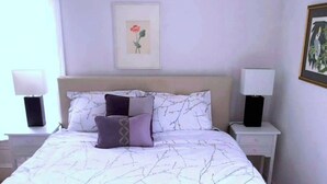 Een netjes opgemaakt bed met een bedsprei met patroon, twee bedlampen en een ingelijst schilderij aan de muur.