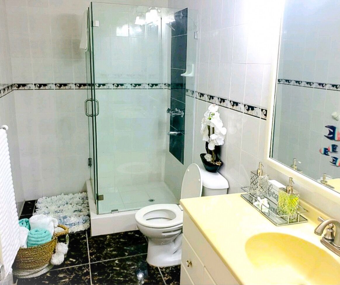 A bathroom with a glass shower enclosure, a toilet, and a sink with a mirror.