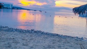 Una spiaggia con mare calmo, un tramonto e una costruzione con tetto di paglia.