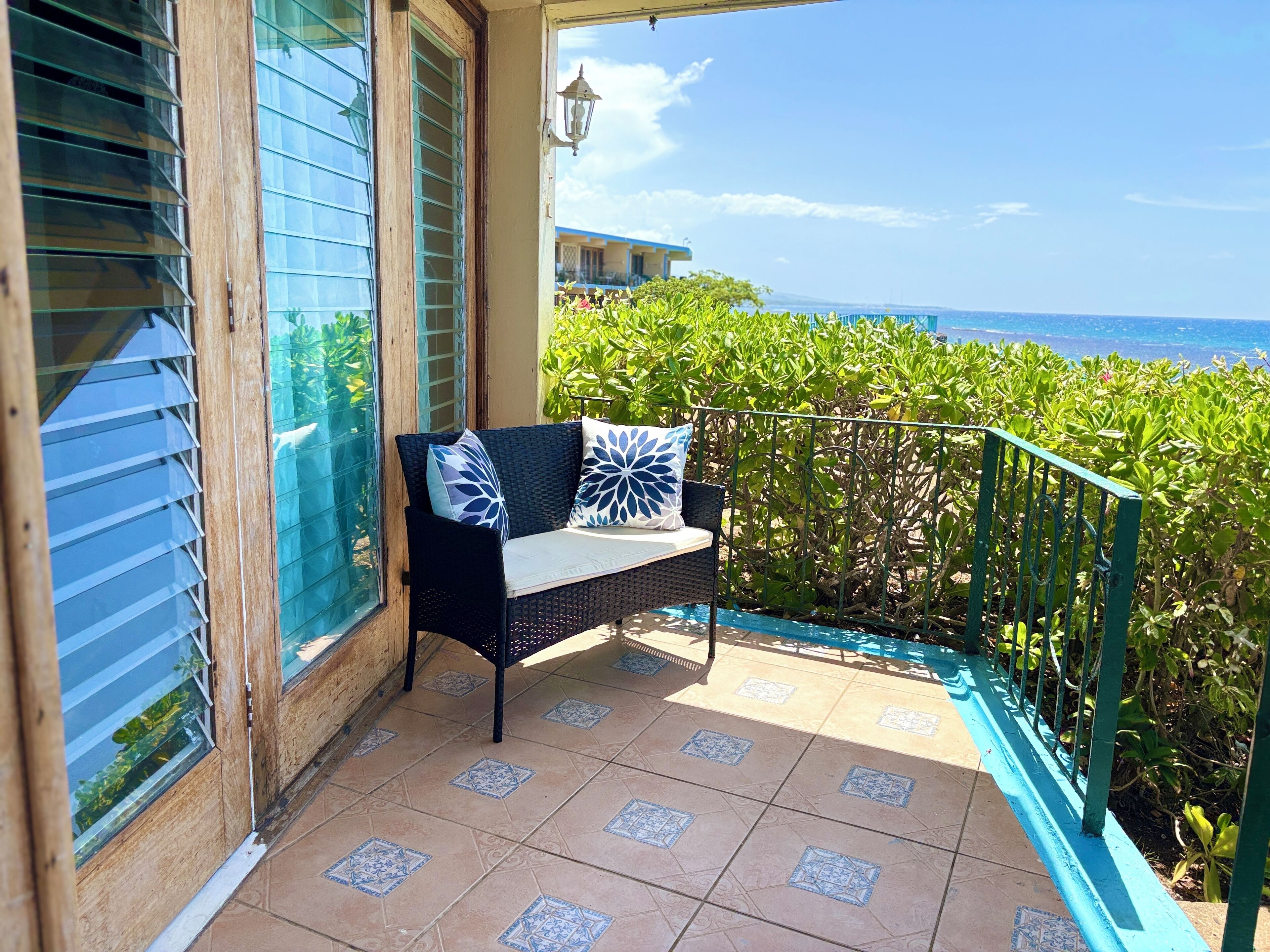 Un balcon avec un canapé en osier, une vue sur l’océan et un sol carrelé.