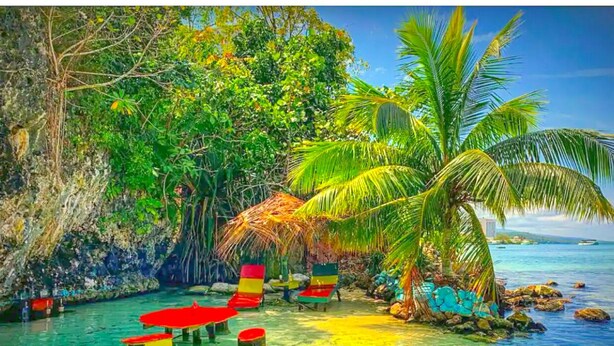 Una spiaggia con acque cristalline turchesi, palme e poltrone rosse da relax.