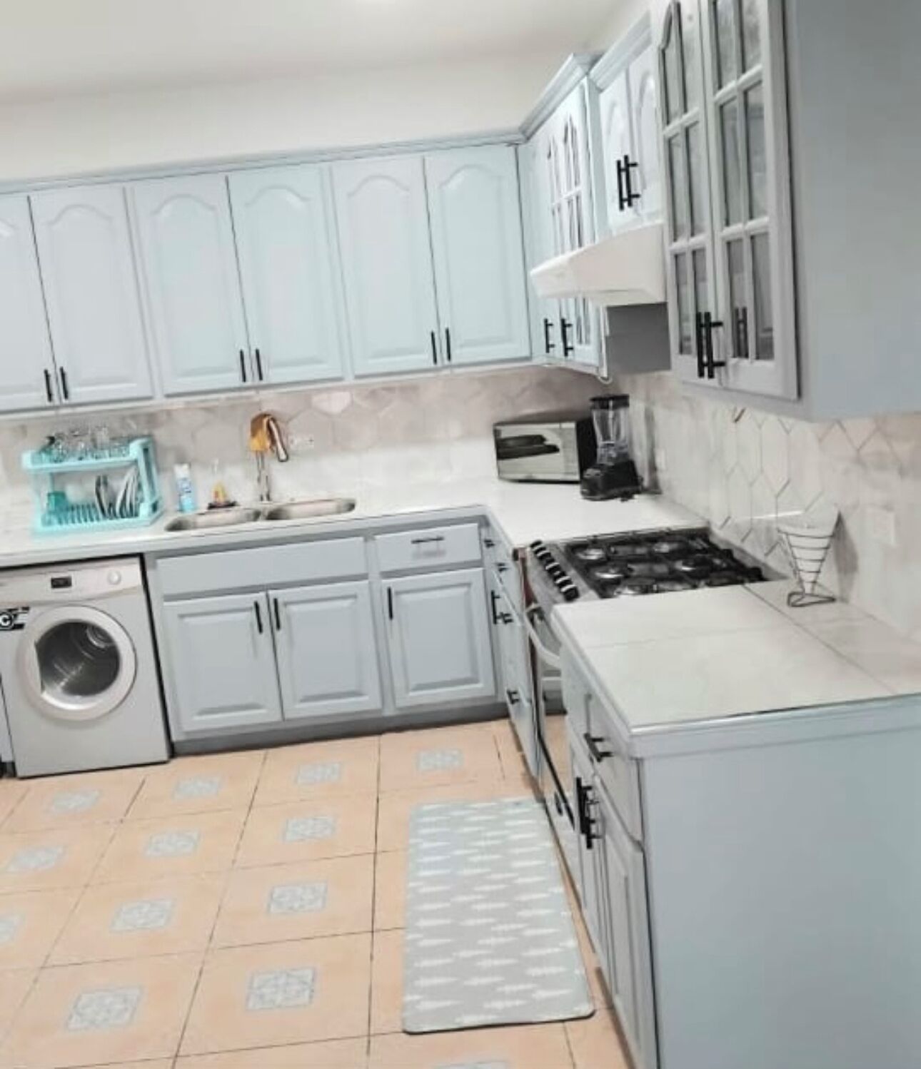 A compact kitchen with grey cabinets, a washing machine, a microwave, and a gas stove.
