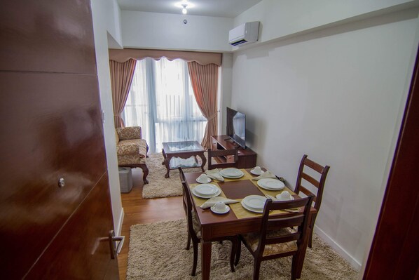 Un área de comedor con una mesa de madera dispuesta para cuatro personas, una televisión y un sofá al fondo.