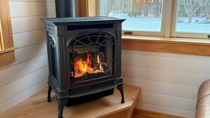 Huoneen nurkassa on puukamiina, ja ikkunasta avautuu näkymä lumiseen maisemaan.