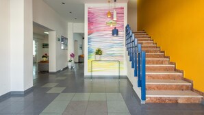 A modern interior with a staircase, a colorful abstract painting, and a reception area. - Flisvos Hotel Tolo (Nafplio)