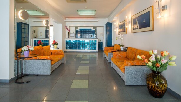 A hotel lobby with orange sofas, a vase of flowers, and a view of the reception area. - Flisvos Hotel Tolo (Nafplio)