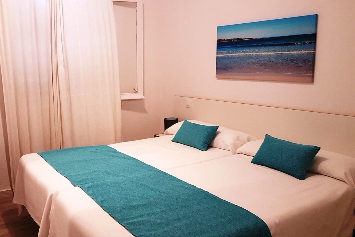 A hotel room with a bed, a painting of a beach, and a nightstand.