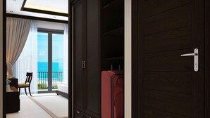 A hotel room with a large wardrobe, a red suitcase, a chair, and a view of the sea through a balcony. - Hoi An Waterway Resort (Hoi An)