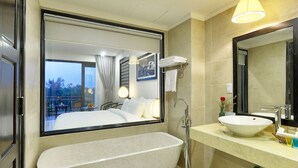 A modern bathroom with a freestanding bathtub, a large mirror, and a vanity with a sink. - Hoi An Waterway Resort (Hoi An)