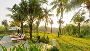 A poolside area with lounge chairs and umbrellas, surrounded by palm trees and lush greenery. - Hoi An Waterway Resort (Hoi An)