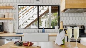 Une cuisine moderne dotée d’une grande fenêtre, d’un plan de travail en bois et offrant une vue sur un escalier et la verdure environnante.