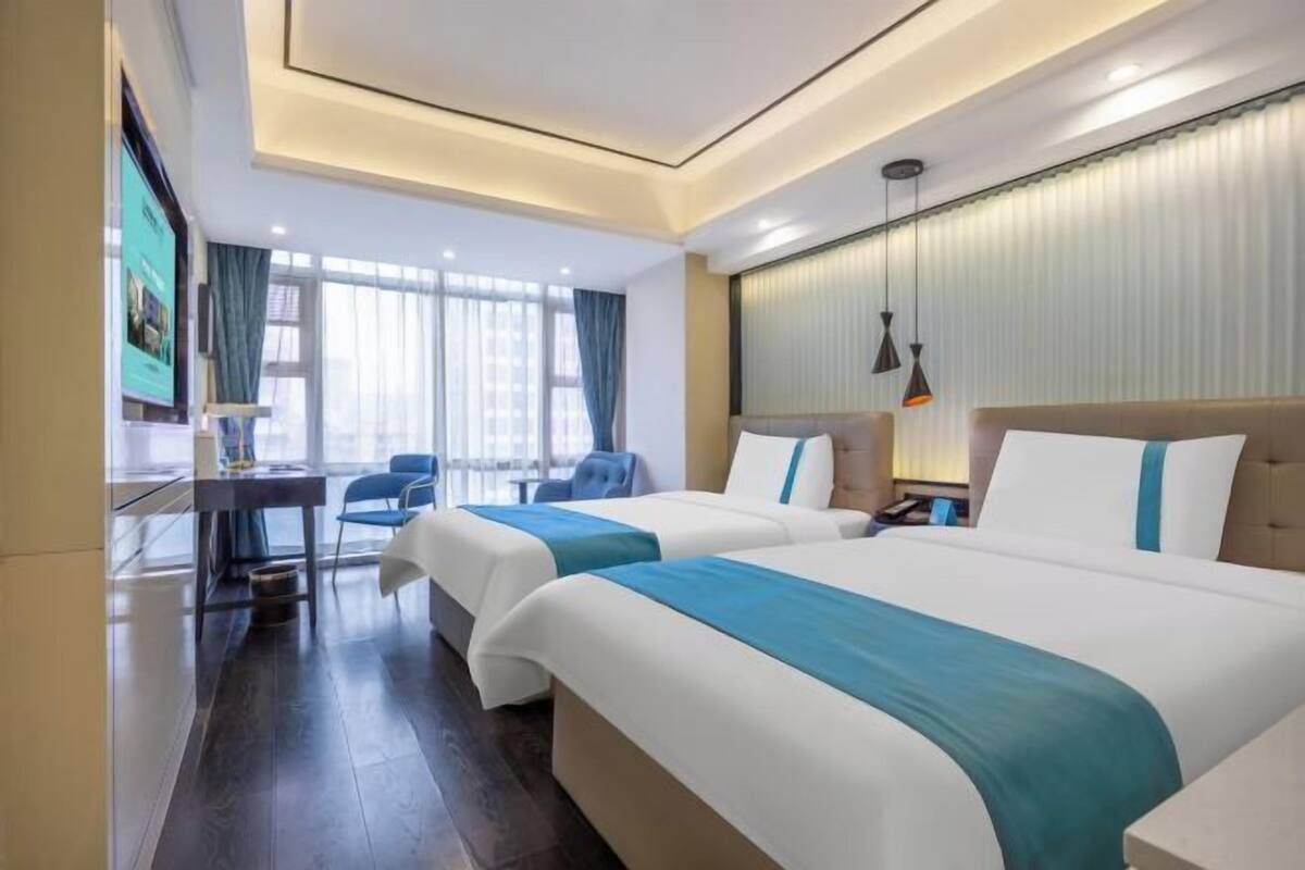 Une chambre d’hôtel avec deux lits, un bureau, une chaise et une grande fenêtre.