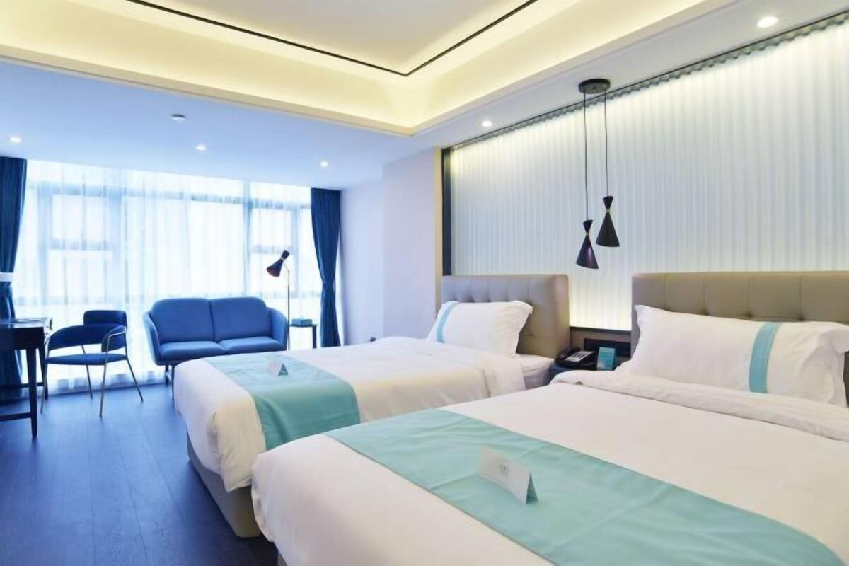 Une chambre d’hôtel avec deux lits, un bureau, une chaise et une fenêtre avec des rideaux.