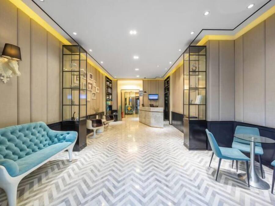 Un hall de hotel con diseño moderno, que incluye un sofá azul, un mostrador de recepción y una zona de estar con sillas y una mesa azules.
