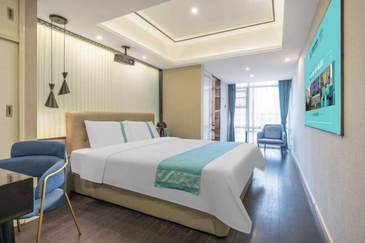 A hotel room with a bed, bedside table, chair, and a view of the hallway.