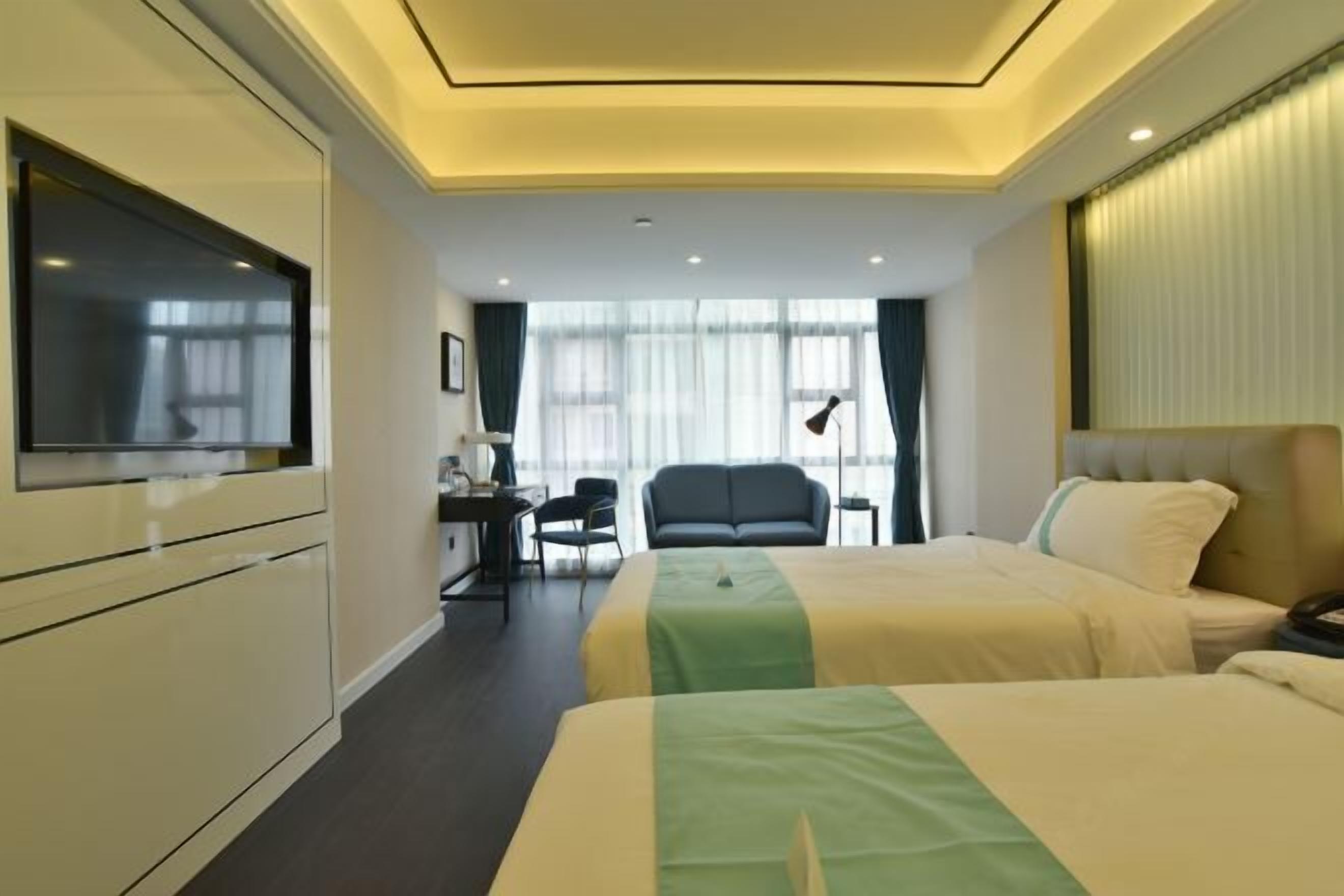 A hotel room with two beds, a desk, a chair, and a TV.