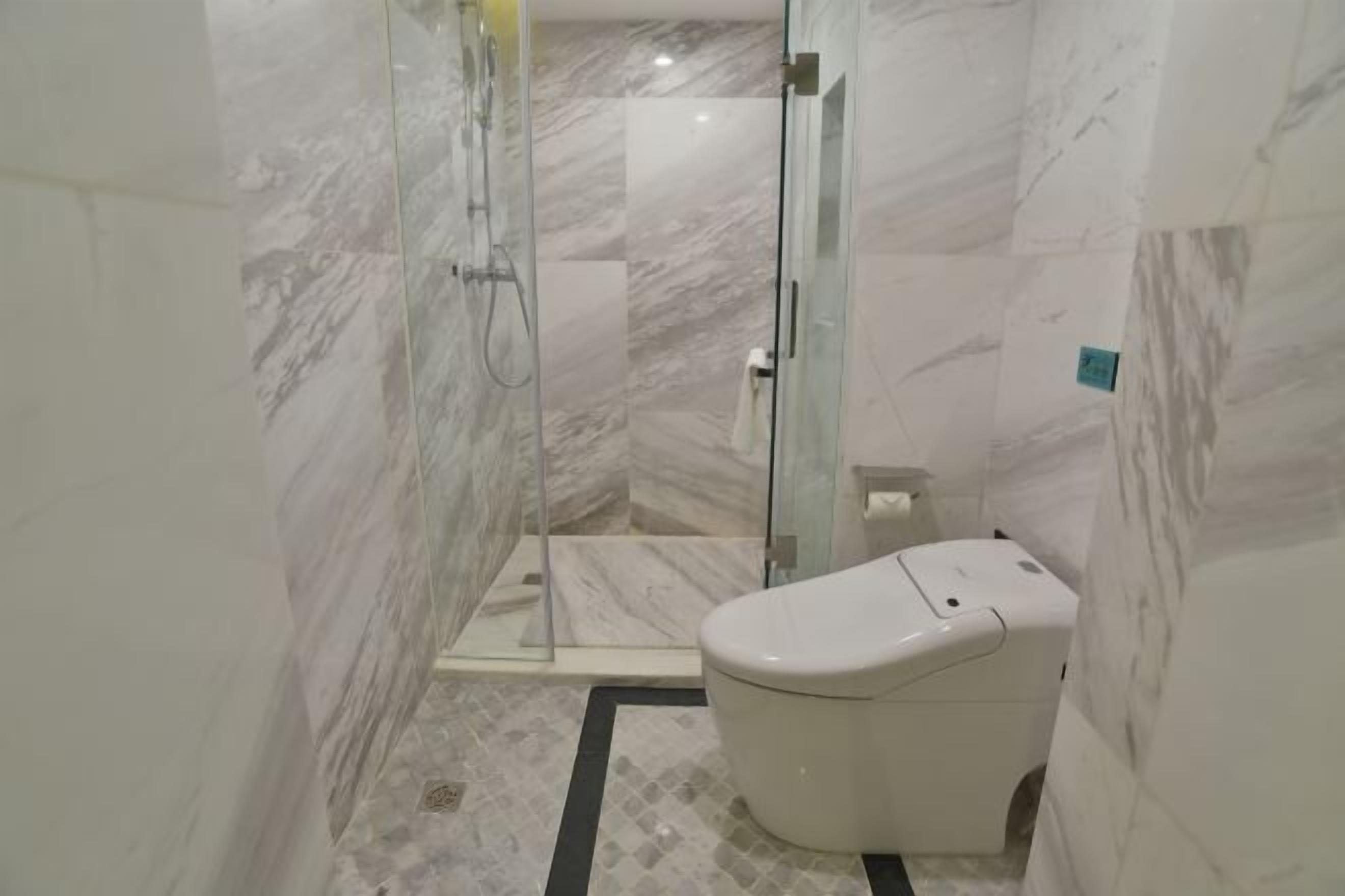 A modern bathroom with a glass-enclosed shower, a toilet, and a marble floor.