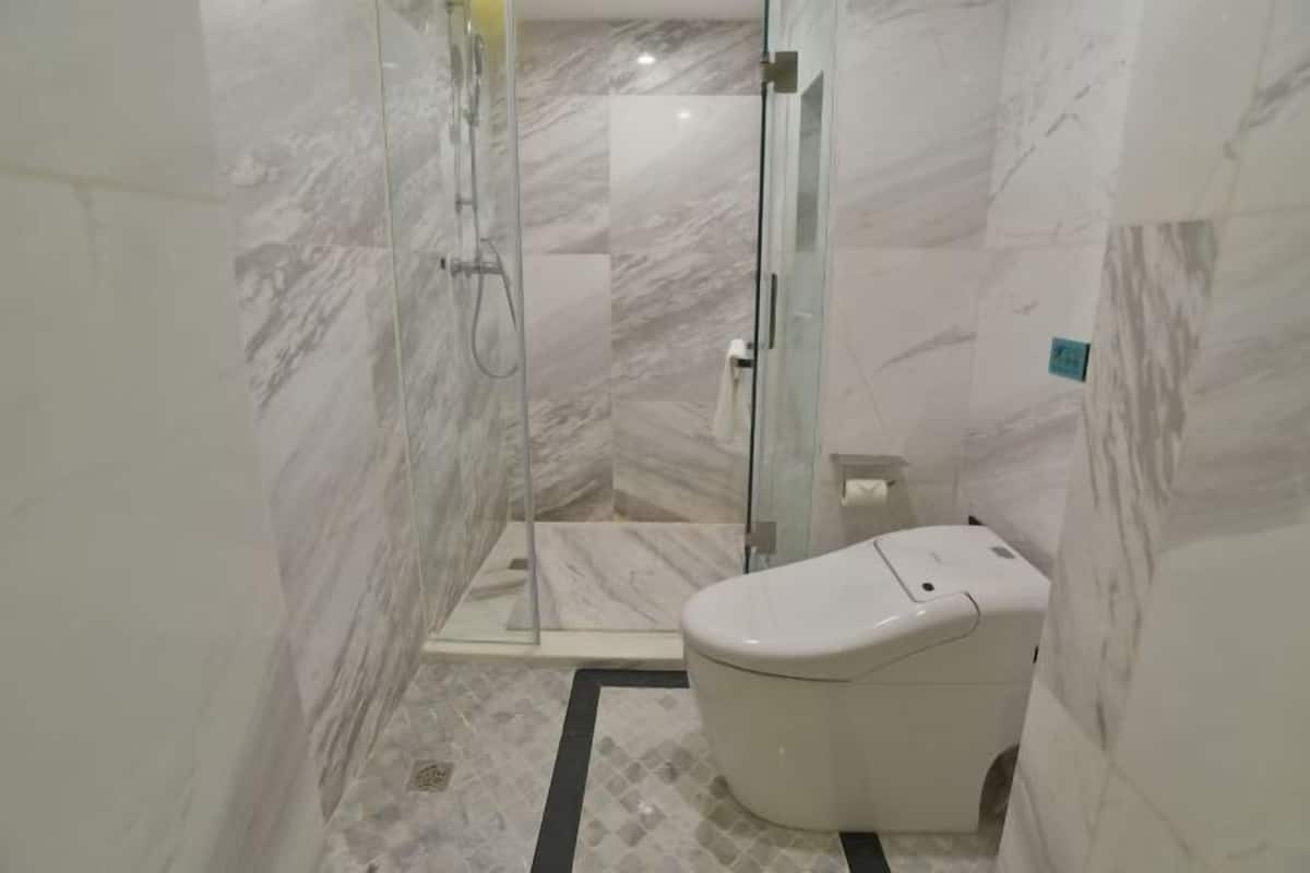 A modern bathroom with a glass-enclosed shower, a toilet, and a marble floor.