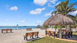 Una spiaggia con panchine di legno, un padiglione con tetto di paglia e vista libera sull'oceano.