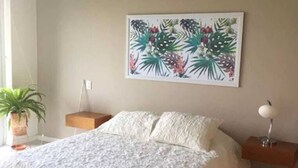 A bedroom with a large bed, a nightstand, a wall-mounted lamp, and a potted plant.