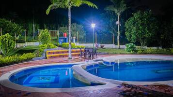 Una piscina de diseño curvo, rodeada por un paseo de ladrillos y palmeras.