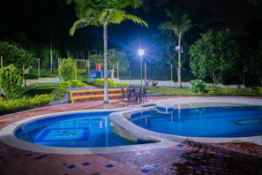 A swimming pool with a curved design, surrounded by a brick walkway and palm trees. - Finca Hotel San Isidro (Calarcá)