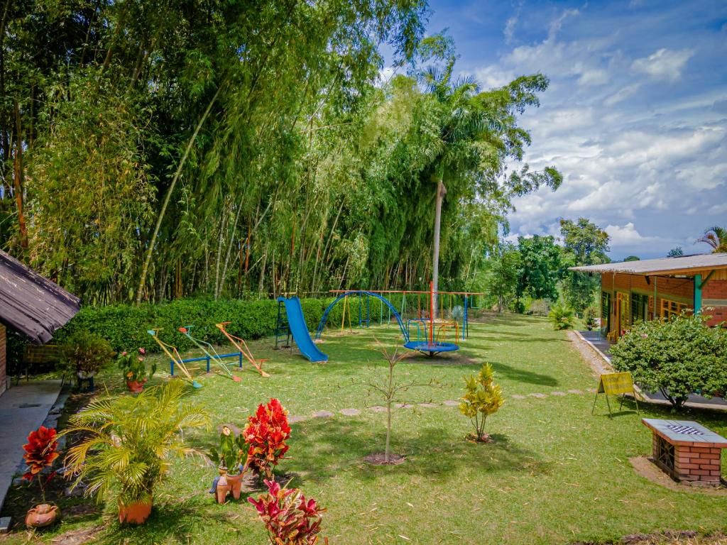 Un exuberante jardín con un parque infantil, que incluye un tobogán y columpios, rodeado de densos árboles de bambú.