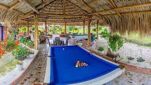 An indoor pool area with a blue pool table, surrounded by potted plants and outdoor seating.
