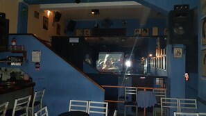 Zona de bar con pantalla de televisión, asientos y una escalera.