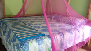 Un letto con copripiumino floreale e coperta a righe, una zanzariera rosa e una testiera in legno.