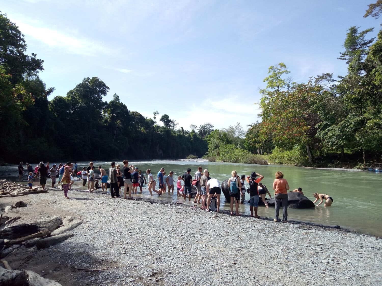 Un groupe de personnes s’était rassemblé au bord d’une rivière, certaines étant debout et d’autres dans l’eau.