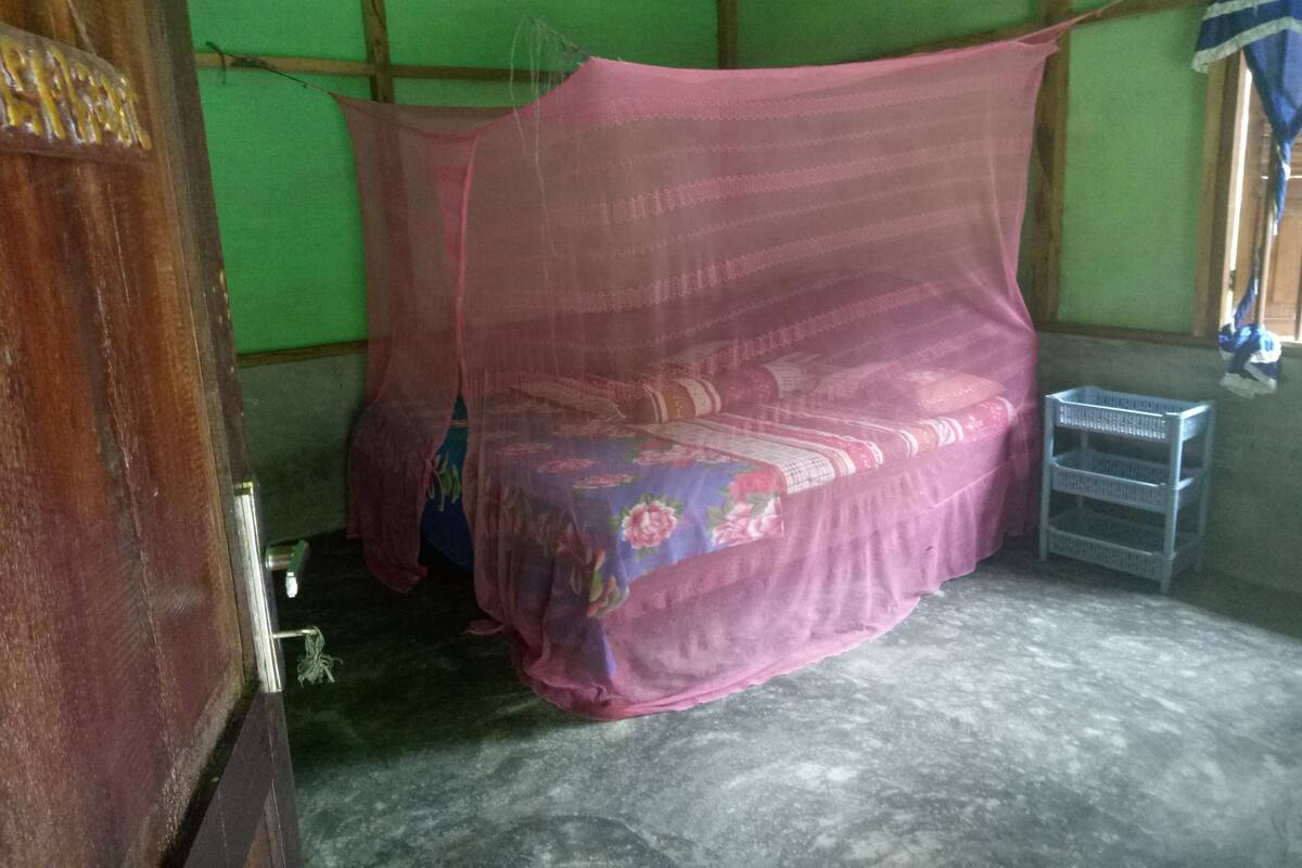 Een kamer met een bed, overdekt met een klamboe, een klein plastic mandje en een groene wand.