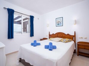 Una habitación de hotel con cama, una ventana con cortinas, una mesita de noche y un cuadro colgado en la pared.