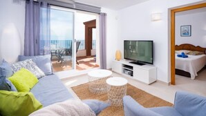 Ein modernes Wohnzimmer mit einer Couch, einem Fernseher und einem Balkon mit Tisch und Stühlen.