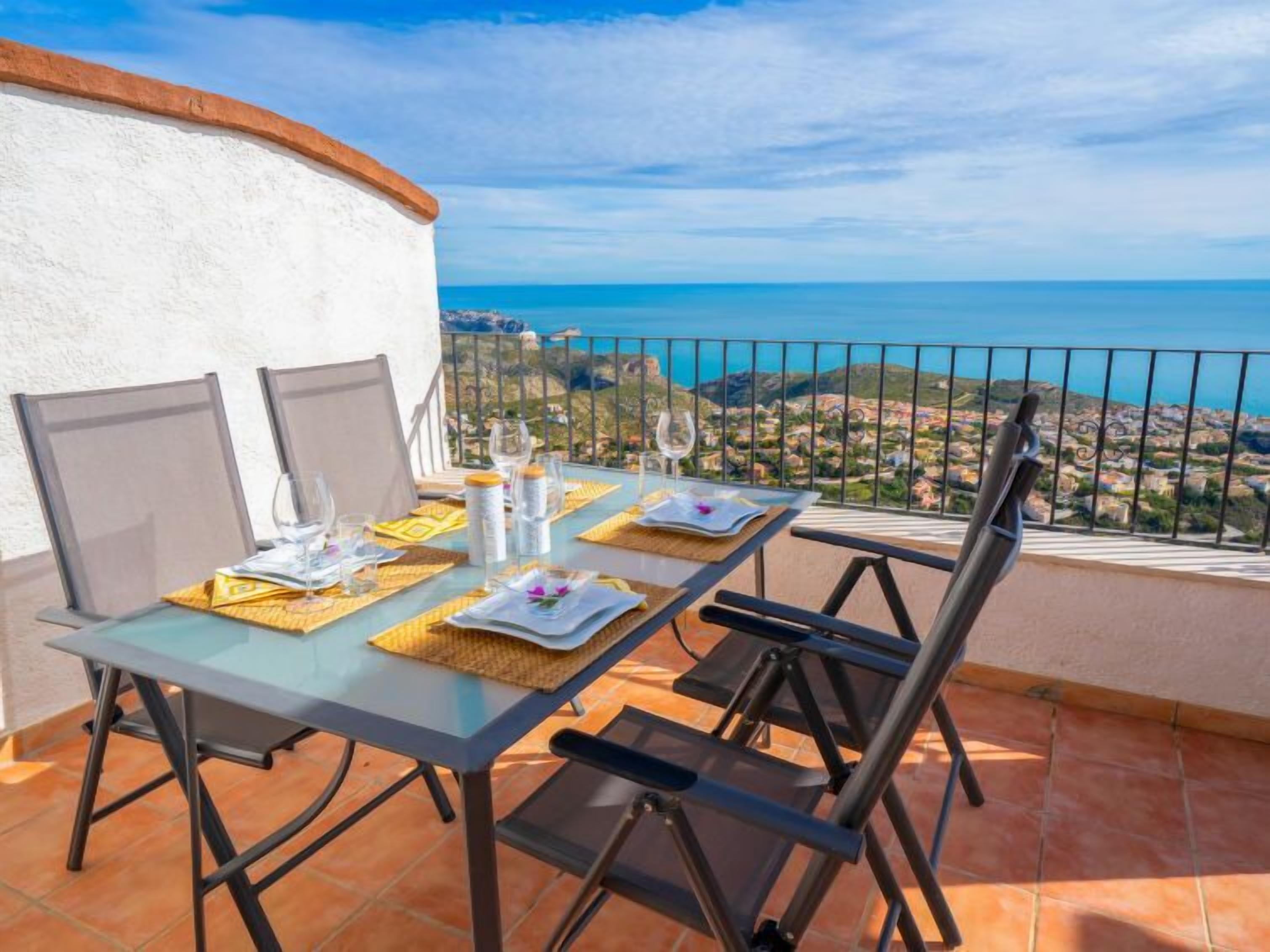 Une table à manger installée sur une terrasse, avec vue sur la mer et une ville en arrière-plan.