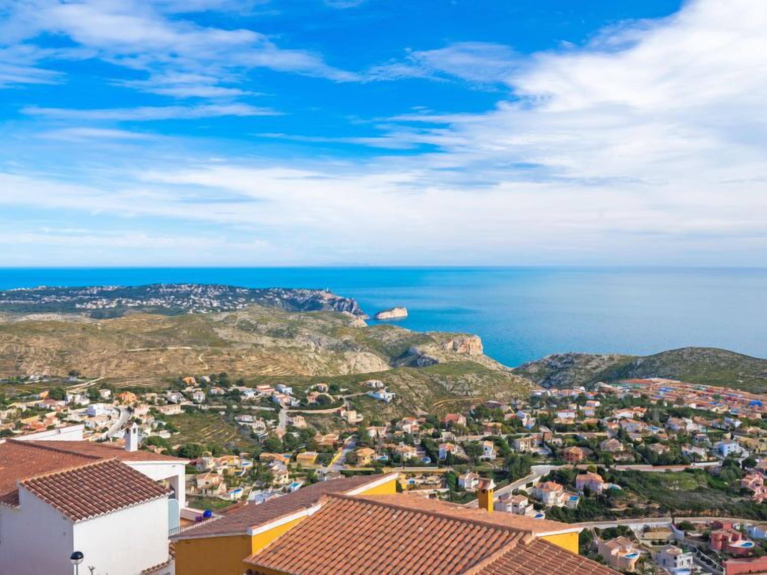 Eine Küstenstadt mit terrassenförmig angeordneten Häusern, freiem Blick auf das Meer und einer markanten Felsformation im Hintergrund.