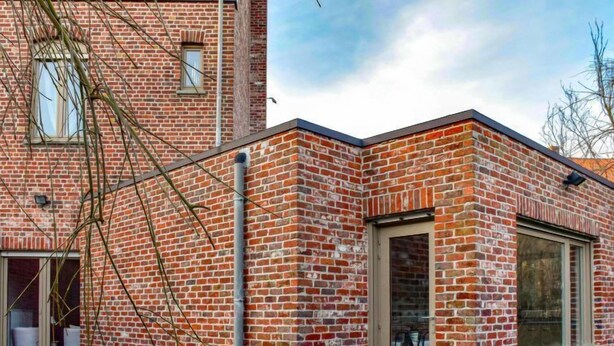 A brick building with a large glass door and windows, a visible chimney, and a small outdoor area with potted plants.