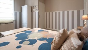 A bedroom with a bed, a dresser, a wardrobe, and a bedside table with a lamp.