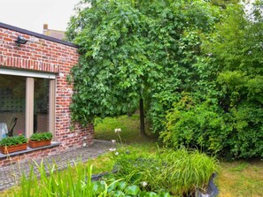 A brick building with a glass door and windows, surrounded by lush greenery and a variety of plants. - Memories by Interhome (Le Bizet)