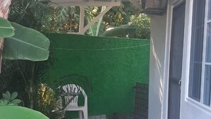 A covered patio area with a brick floor, a green wall, and a white chair. - Centrally located room, in a house with free Wifi. (Port Antonio)