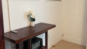 A room with a flat-screen TV mounted on the wall, a wooden TV stand with a small white vase, a framed picture of a cove, and a white door. - Centrally located room, in a house with free Wifi. (Port Antonio)