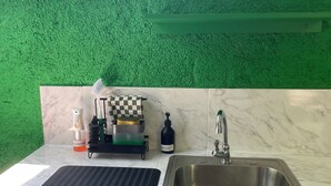 A kitchen with a green textured wall, a marble countertop, a stainless steel sink, a checkered cloth, a soap dispenser, and a dish rack. - Centrally located room, in a house with free Wifi. (Port Antonio)