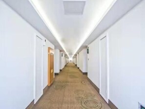A long, narrow hotel corridor with doors on both sides, carpeted flooring, and overhead lighting.