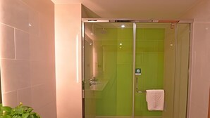 A glass-enclosed shower with green tiles, a white towel hanging on the door, and a plant on the counter. - Greentree Inn Tongxiang Chongfuzhen World Fur Cent (Jiaxing)