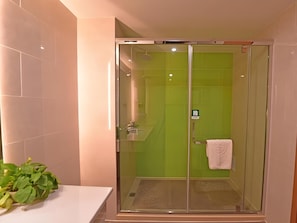 A glass-enclosed shower with green tiles, a white towel hanging on the door, and a plant on the counter. - Greentree Inn Tongxiang Chongfuzhen World Fur Cent (Jiaxing)