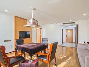 A hotel room with a dining table, chairs, a television, a sofa, and a wooden floor. - Greentree Inn Tongxiang Chongfuzhen World Fur Cent (Jiaxing)