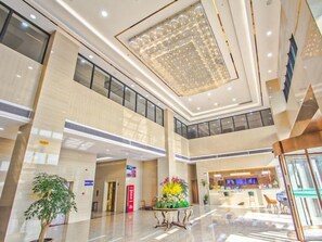 Un hall d’entrée spacieux avec un plafond haut, un comptoir de réception et un coin salon agrémenté d’une plante.