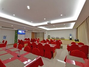 Une salle de conférence équipée de plusieurs tables et chaises, d’un écran de projection et d’un téléviseur.