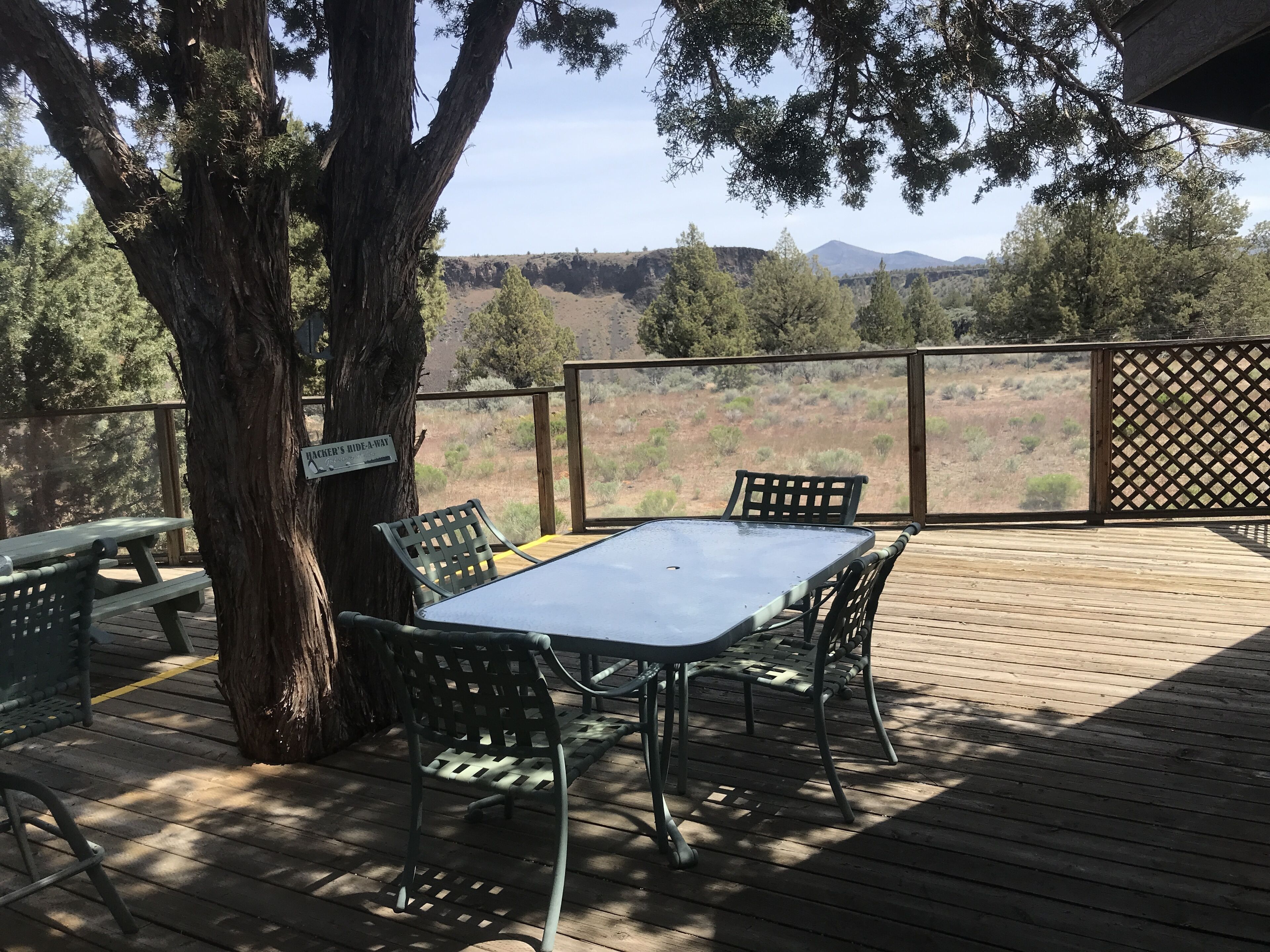 Een terras buiten met een tafel en stoelen, een picknicktafel en een bord met de tekst 'Hiker's Bide-a-way'.