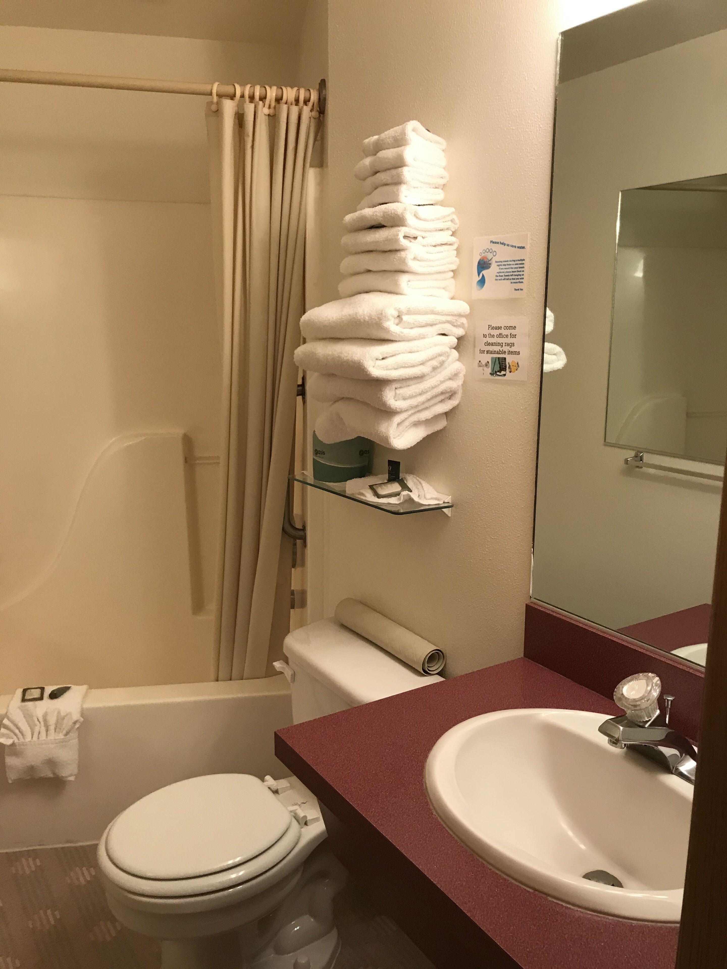 Een badkamer met toilet, wastafel en douchegordijn. Er liggen handdoeken op een plank en is een bordje met informatie over schoonmaakdoeken.